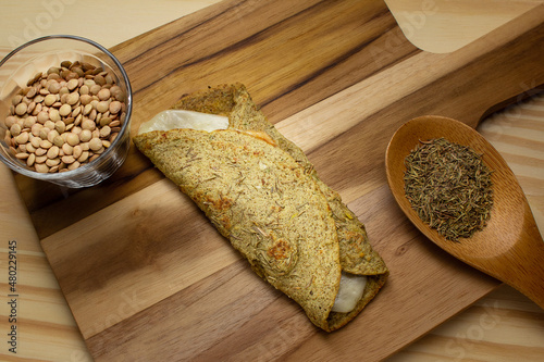 Panqueca de lentilhas com recheio de mussarela, uma colher de madeira com tomilho, um copo com lentilhas cruas, sobre uma tábua de madeira. photo