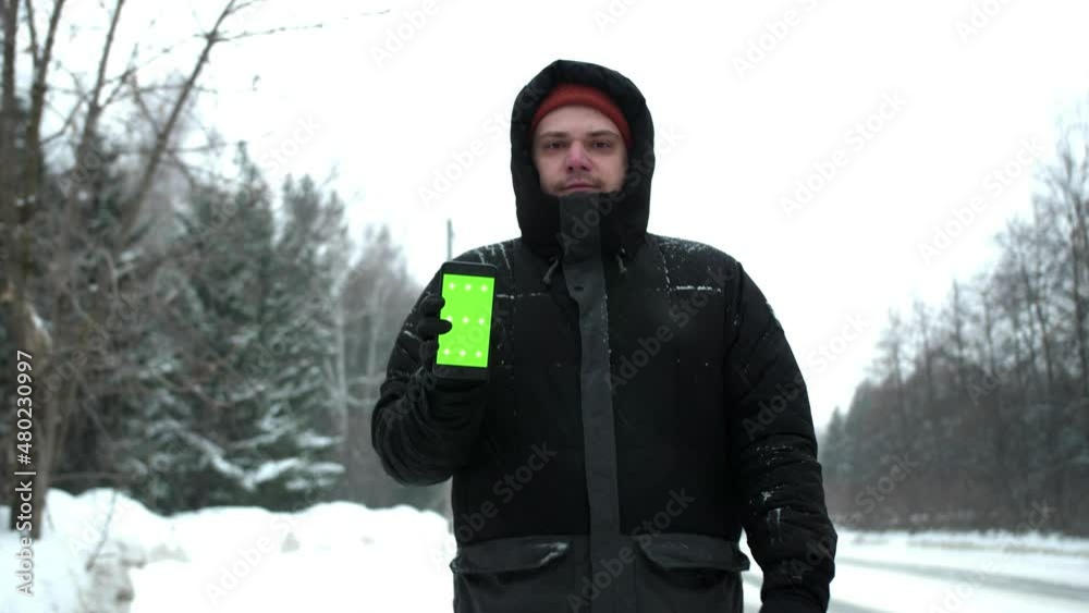 A man goes to the camera in the winter and shows the phone with a green screen. Shooting during snowfall. A man goes to the camera in the winter and shows the phone with a green screen. Shooting during snowfall.