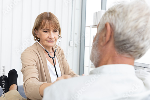 senior woman doctor on home visit and examining elderly man patient by stethoscope