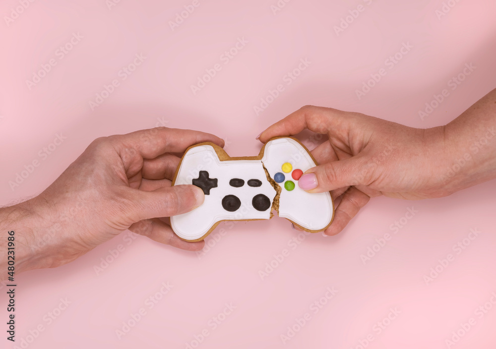 A man's and a woman's hand are tearing apart a gamepad-shaped gingerbread. Competition concept A man's and a woman's hand are tearing apart a gamepad-shaped gingerbread. Competition concept