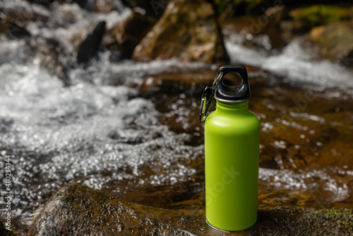 Camping steel bottle of water on a stone near mountain river