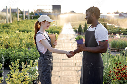 Male and female multiracial engineers shaking hands after successful inspecting greenhouse organic farm business construction. Multi-sex farmers. happy Man and woman. Agronomy concept