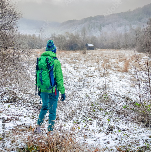 Obraz na płótnie tourist backpacker traveler with a green backpack goes on a trekking route in the winter in the forest in frosty weather w salonie