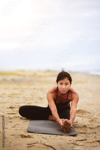 A portrait of beautiful woman stretching her arms and legs on the beach. Yoga sport. Healthy wellness lifestyle. Spiritual health. Personal fulfillment.
