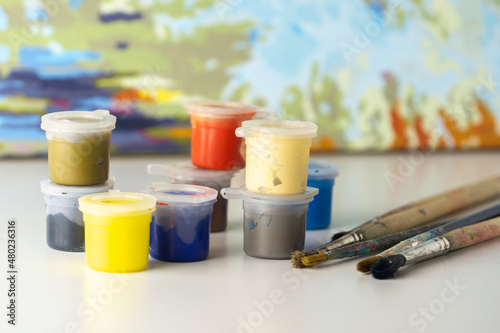 Bright multi-colored jars of paint for drawing by numbers. Paints and brushes on a blurred watercolor background. The concept of creativity, drawing lessons.