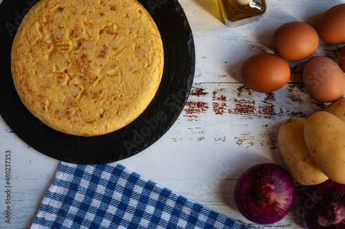 Traditional Spanish omelette and the ingredients for its preparation on a wooden table. Aerial view