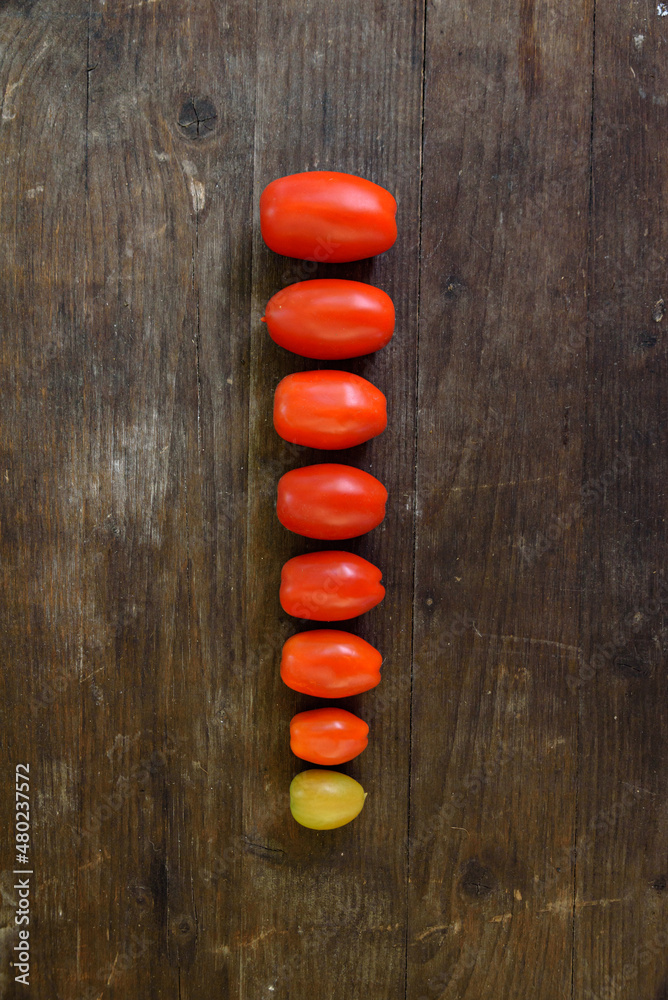 Some ripe red tomatoes lined up on an old wooden table. Concept of status bar, charging bar, increasing progression, the smallest, the largest. Some ripe red tomatoes lined up on an old wooden table. Concept of status bar, charging bar, increasing progression, the smallest, the largest.