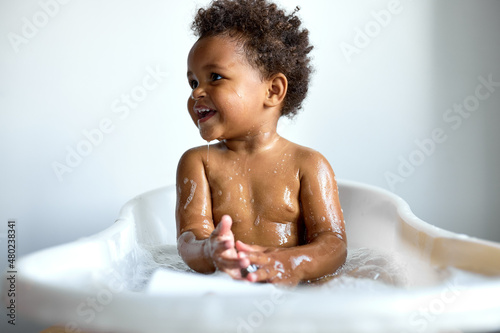 Fotografering happy black child sitting in bath with foam