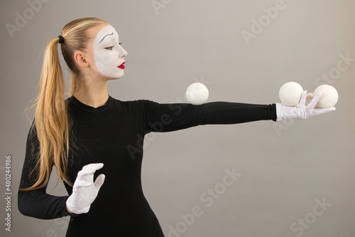 The mime artist juggles balls. Circus clown woman. On a gray background.