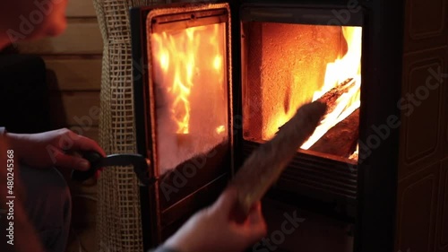POV hands open stove door and put firewood into flame in furnace of potbelly stove, then close fireplace door. Cozy winter fireplace with burning firewood behind transparent stove door photo