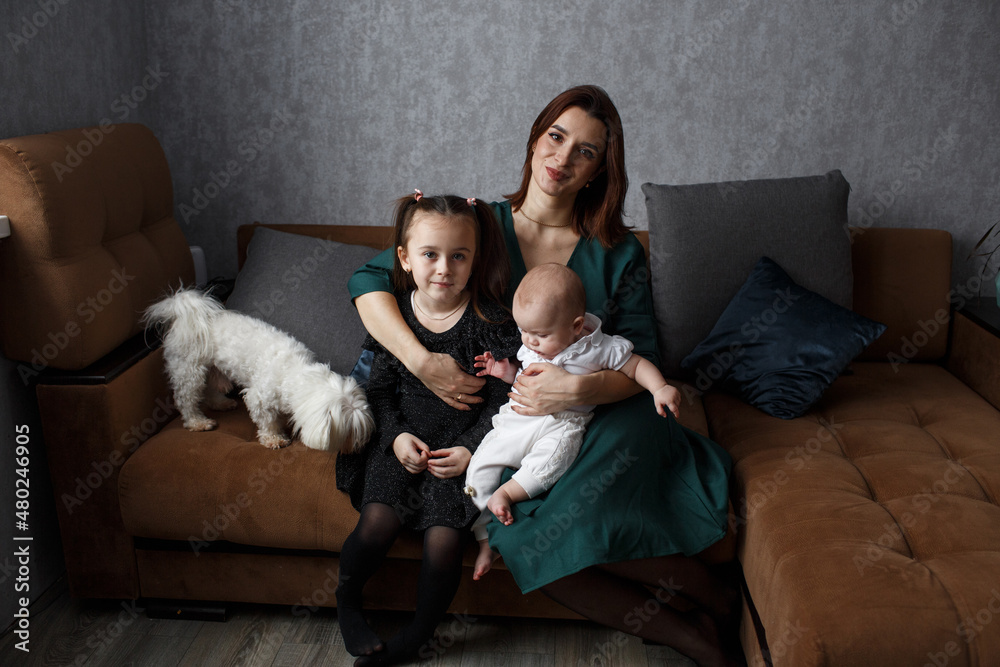 A happy young mother is sitting on the couch with young preschool children, hugging, enjoying the weekend together A happy young mother is sitting on the couch with young preschool children, hugging, enjoying the weekend together