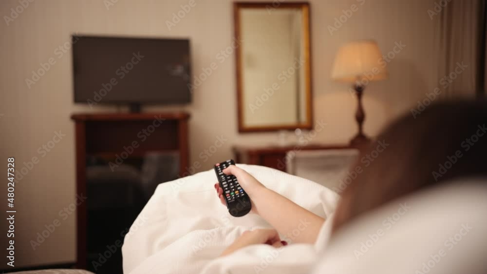 Young woman in casual clothes lying on bed, watching tv. Tired female watching Young woman in casual clothes lying on bed, watching tv. Tired female watching