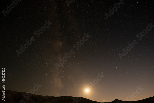 Bright milky way galaxy and moon behind hill silhouette.Night starry sky background.