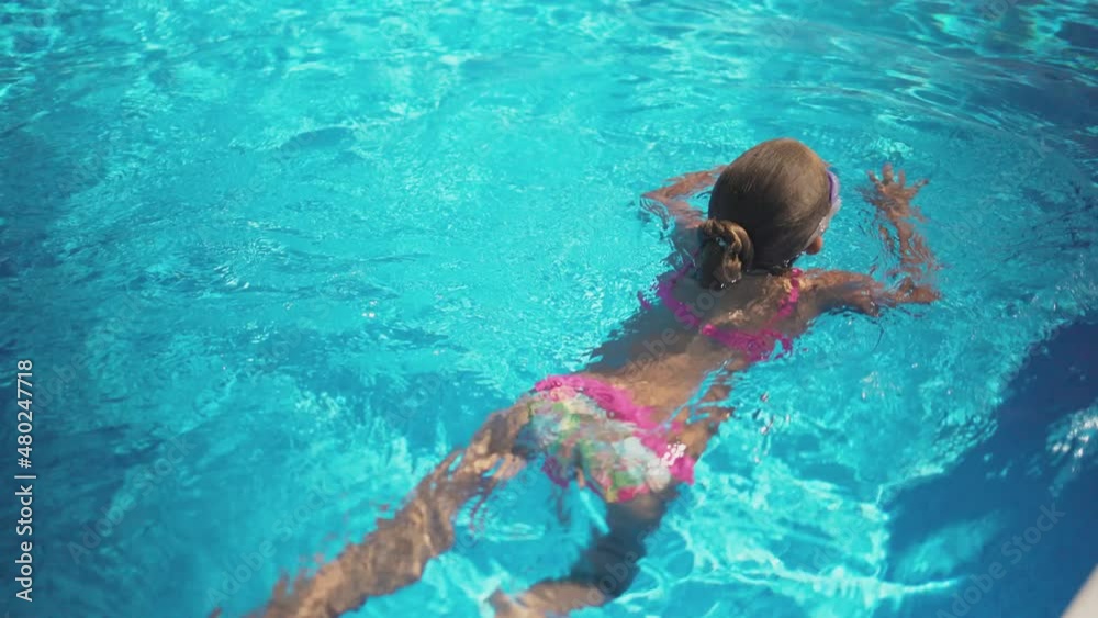 A girl in a pink bathing suit in purple glasses floats on a pool with blue water on a summer day