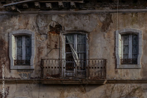 Casona abandonada en ruinas con el balcón con las cortinas saliendo por los cristales rotos y dos ventanas photo