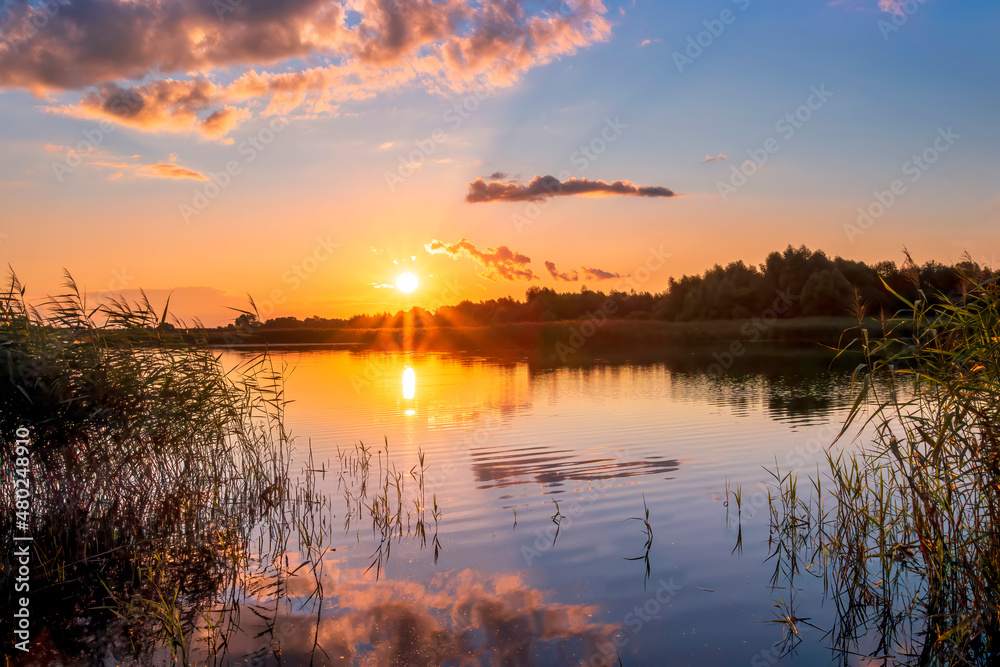 Obraz premium Beautiful scenic view at nice landscape on a beautiful lake and colorful sunset with reflection on water with green gras on foreground and glow on a background, spring season landscape
