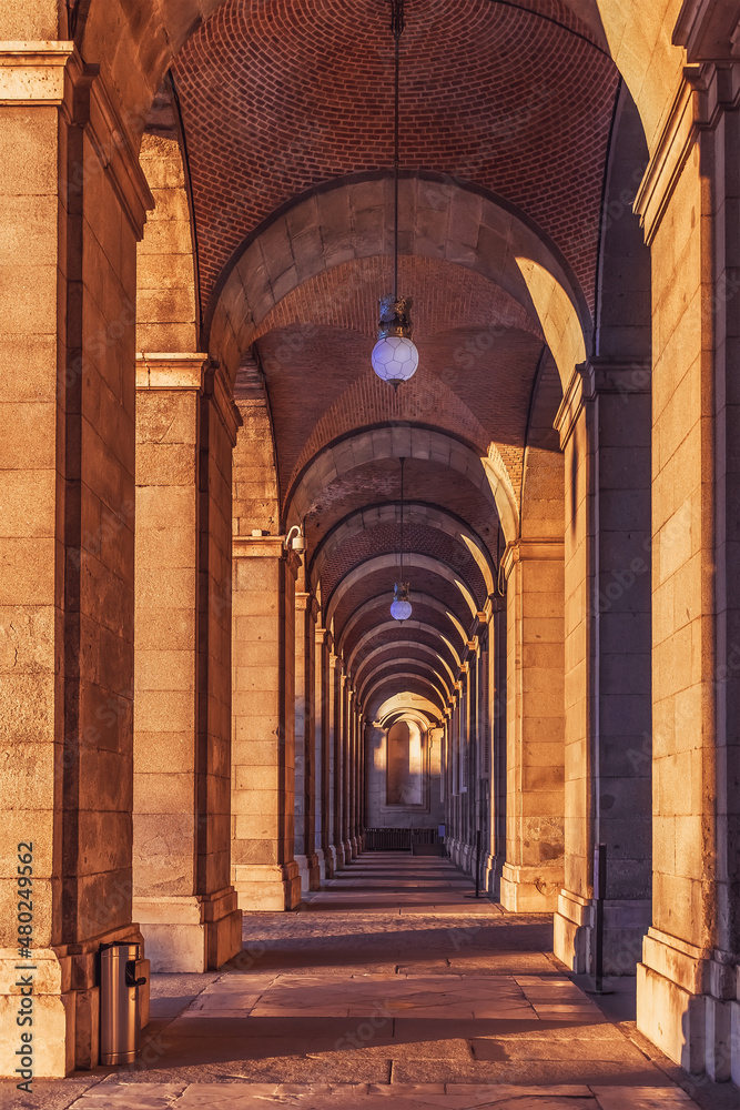 Outdoor arched corridor with columns in the Royal Palace of Madrid, Spain. Vertical architectural background with symmetrical outgoing perspective at sunset