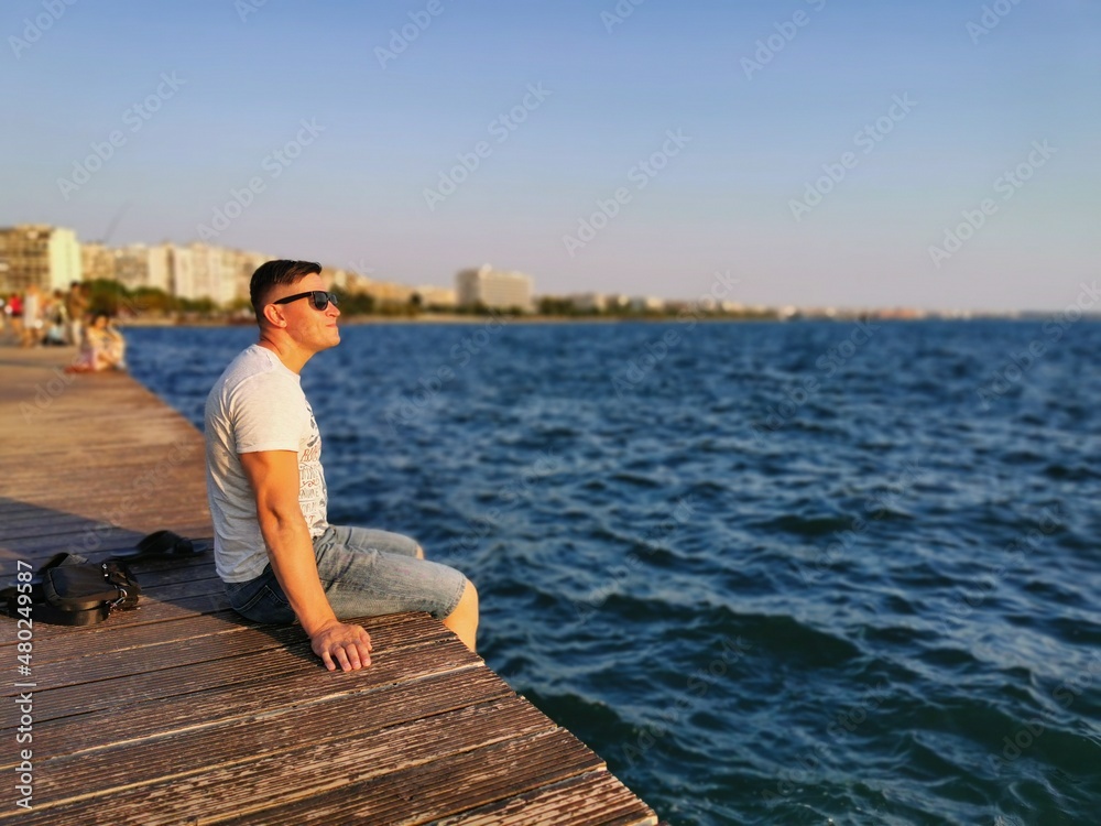 Portrait of a young, athletic man sitting on the edge of the embankment by the sea. He enjoys the sunset and the surrounding nature. Travel, vacation, Greece
Portrait of a young, athletic man sitting on the edge of the embankment by the sea. He enjoys the sunset and the surrounding nature. Travel, vacation, Greece