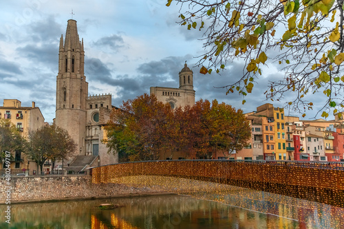 Autumn evening landscape of Girona with Sant Feliu Pedestrian Bridge over Onyar River on the backdrop of Church of St. Felix towers, Spain. Bright cityscape with festive lights reflected in the water photo