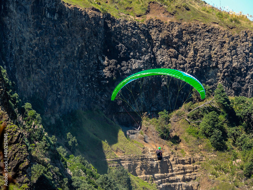 Para glider soars over the beach, waves and hills at Murawai Beach, Auckland, New Zealand photo