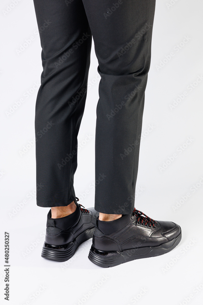 Stylish leather black short men's autumn sneakers on a white background on men's legs. Sneakers winter collection 2022. Stylish leather black short men's autumn sneakers on a white background on men's legs. Sneakers winter collection 2022.