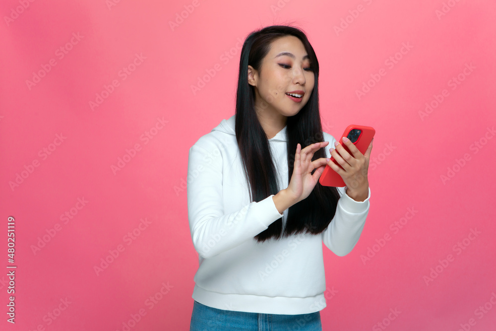 Smiling young asian girl looking at mobile phone screen, chatting in social media, shopping online on pink background Smiling young asian girl looking at mobile phone screen, chatting in social media, shopping online on pink background