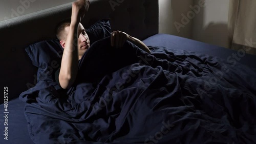 A young handsome guy is engaged in self-satisfaction. In bed at night before going to bed