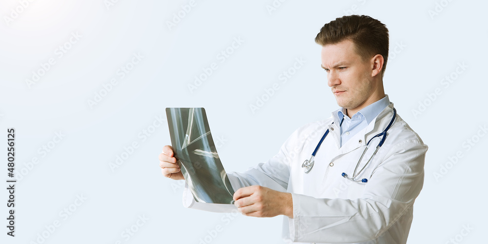 Portrait of cheerful young medical doctor with stethoscope looking at x-ray isolated over grey color background Portrait of cheerful young medical doctor with stethoscope looking at x-ray isolated over grey color background