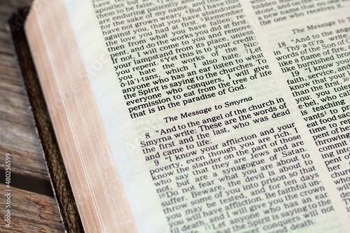 The message to Smyrna Church from God Jesus Christ, an open Holy Bible Book Revelation on wooden background. Christian biblical concept of warning to believers. A close-up.