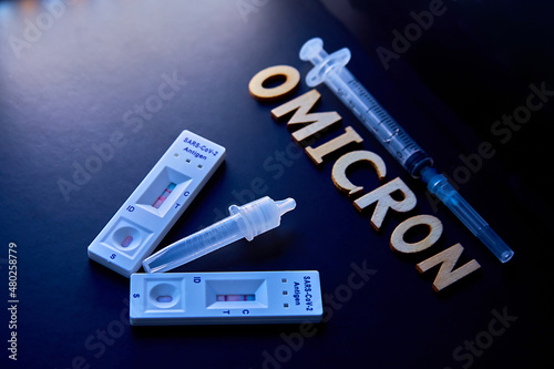 word omicron made from wooden letters,syringe, medical injection bottle and 2 covid-19 antigen self-tests positive on black background.concept-Mutated coronavirus SARS-CoV-2 flu disease pandemic photo