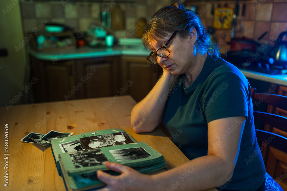 Fototapeta premium Middle aged woman looking at family photo album. Nostalgia, sadness, grief and memories at middle age concept.