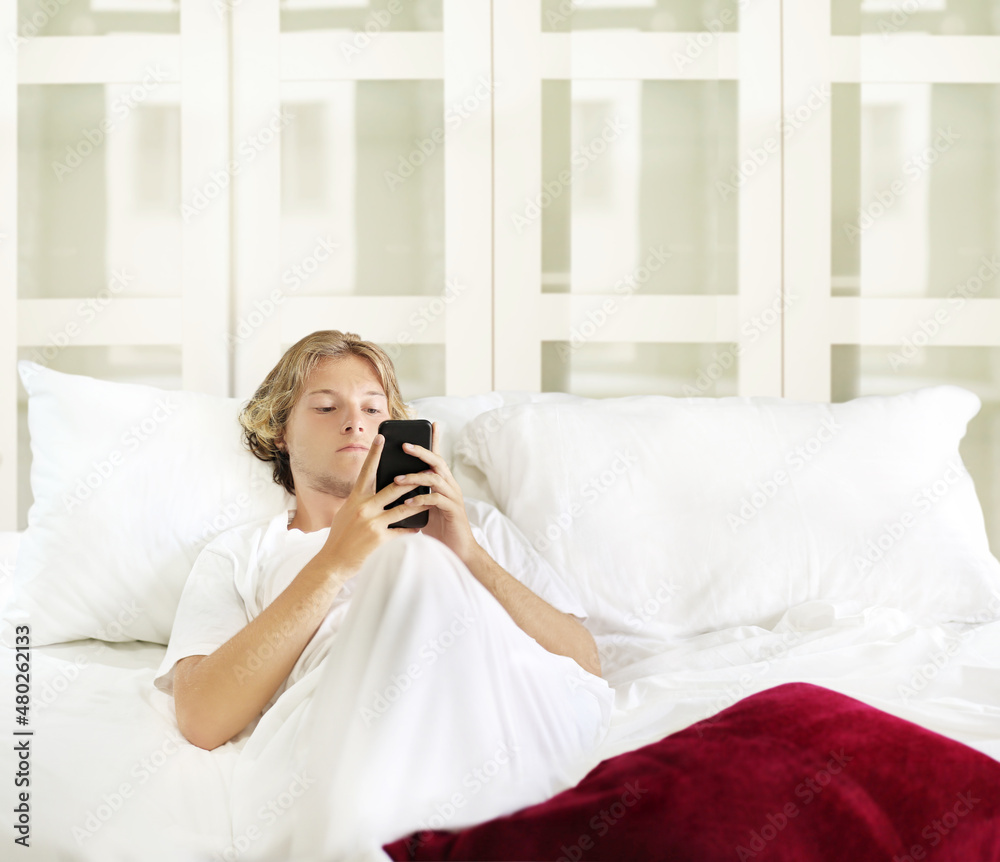 Young man relaxing on bed,using smartphone Young man relaxing on bed,using smartphone