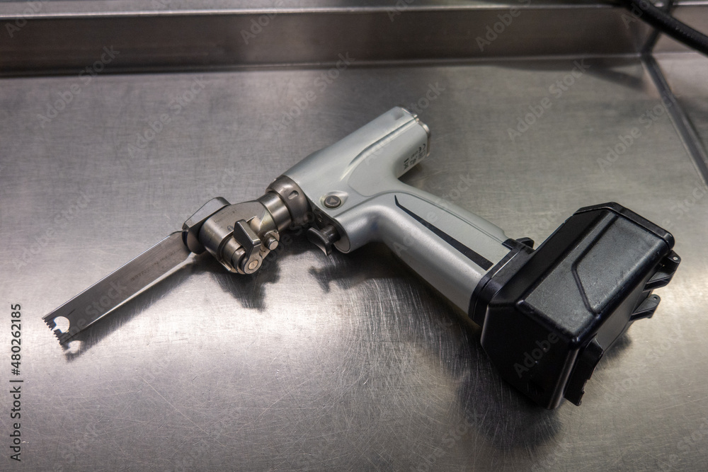 a battery powered surgical oscillating saw with saw blade lies on a green surgical drape