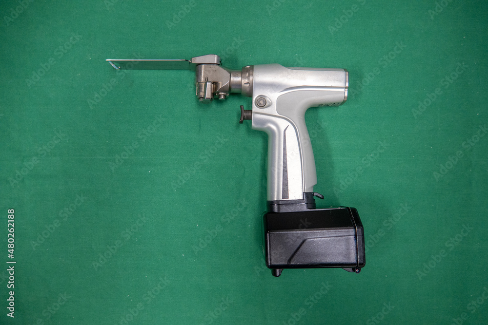a battery powered surgical oscillating saw with saw blade lies on a green surgical drape