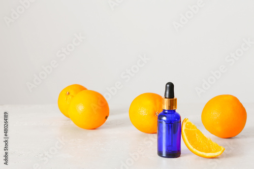 Bottle of essential oil and fresh orange on light background