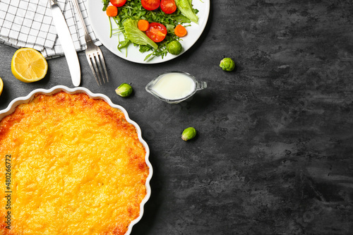 Baking dish with tasty English fish pie on black background, closeup photo