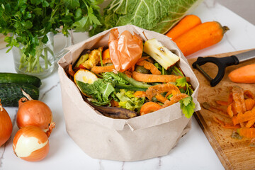 Vegetable and fruit peels, scraps from food preparation collected in trash-pack for recycling. Sorted kitchen waste in paper eco bag on kitchen counter top. Compost-container. Sustainable life style. 