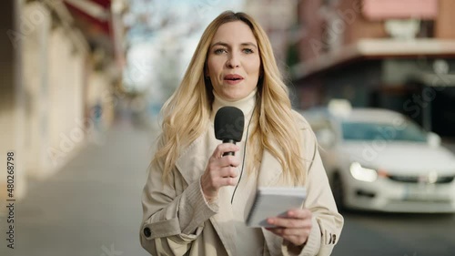Young blonde woman journalist speaking using microphone at street photo