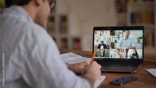 Video call, online conference using app and laptop. Over shoulder view of student or freelancer, studies or works remotely, watches an online lecture, takes notes, multiracial people on laptop screen photo