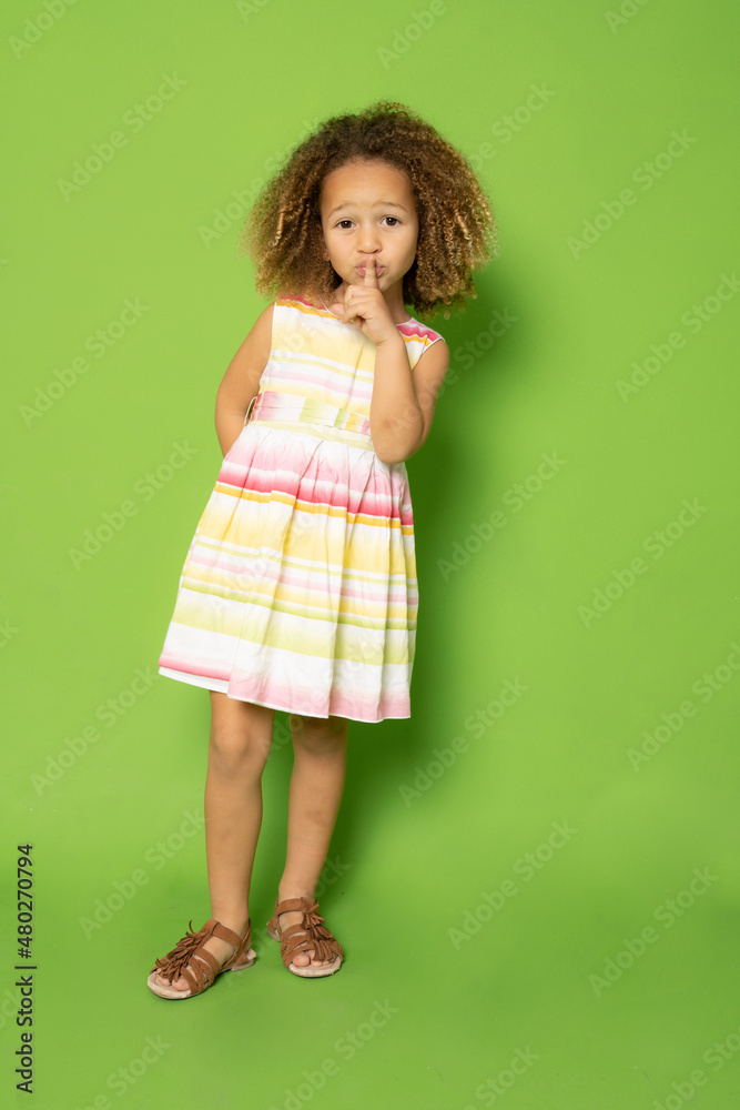 Full length photo of cute little girl with curly hair making silence gesture standing isolated over green background. Full length photo of cute little girl with curly hair making silence gesture standing isolated over green background.
