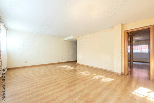 Large empty living room with entrance to a bedroom with light oak hardwood flooring