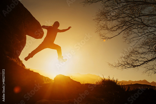 silhouette of man jumping between the rocks of a mountain while hiking in the mountains at sunset. healthy lifestyle