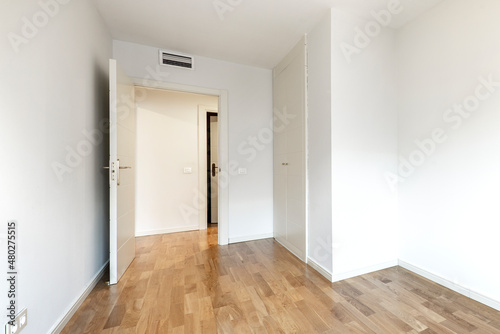 Empty bedroom with fitted wardrobe with white doors and painted walls with oak parquet flooring