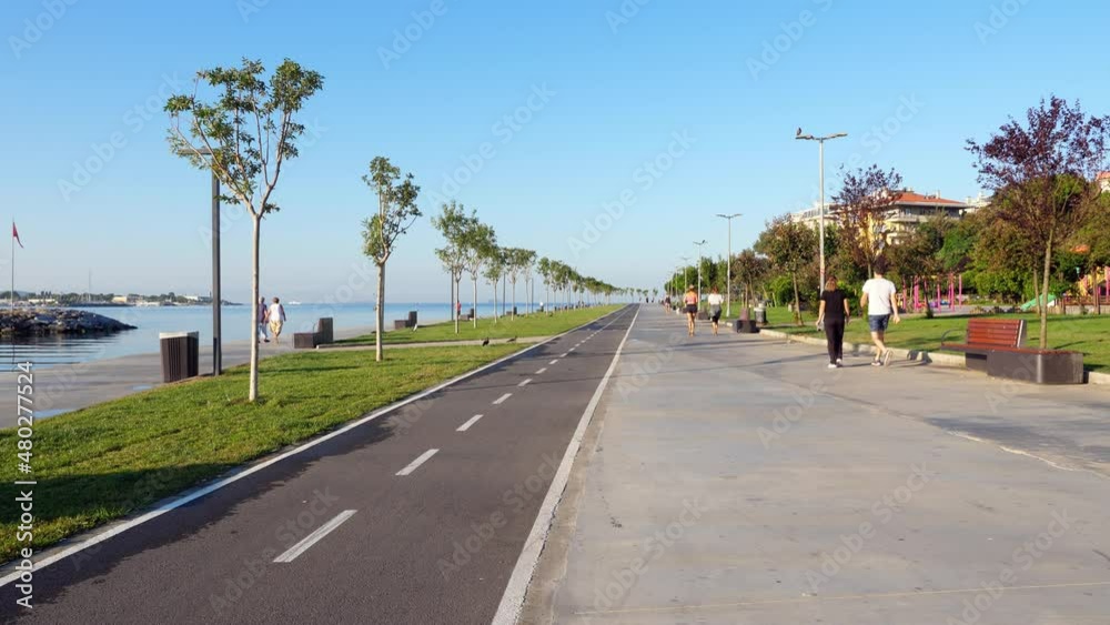 Quite an empty waterfront park, with few people strolling and running along the water in the early hours of the morning. Sunny view of the straight alley and cycle path of Kurbagalidere park
