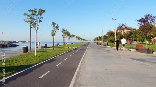 Quite an empty waterfront park, with few people strolling and running along the water in the early hours of the morning. Sunny view of the straight alley and cycle path of Kurbagalidere park photo