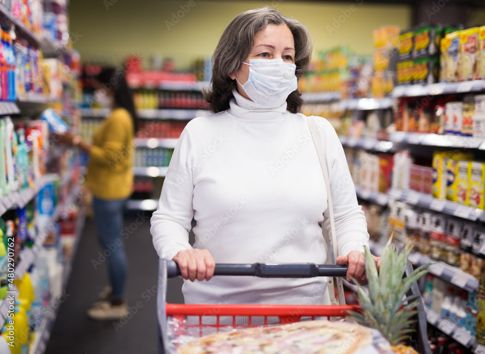Elderly woman in protective face mask shopping in grocery store during pandemic. Concept of new life reality and precautions..