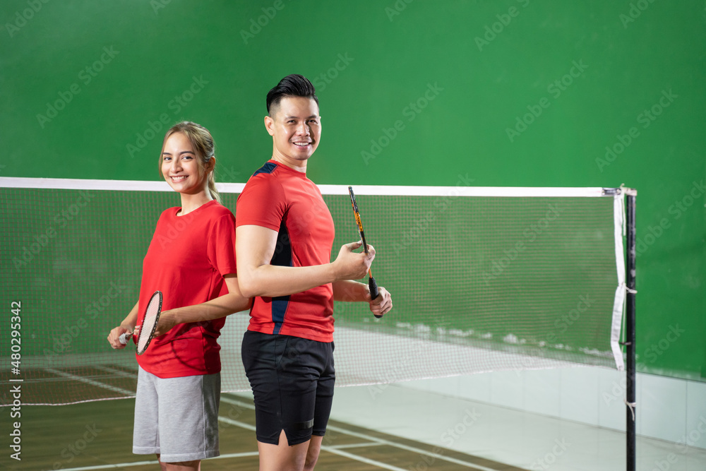 Two smiling badminton players holding rackets standing back to back