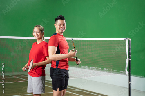 Two smiling badminton players holding rackets standing back to back