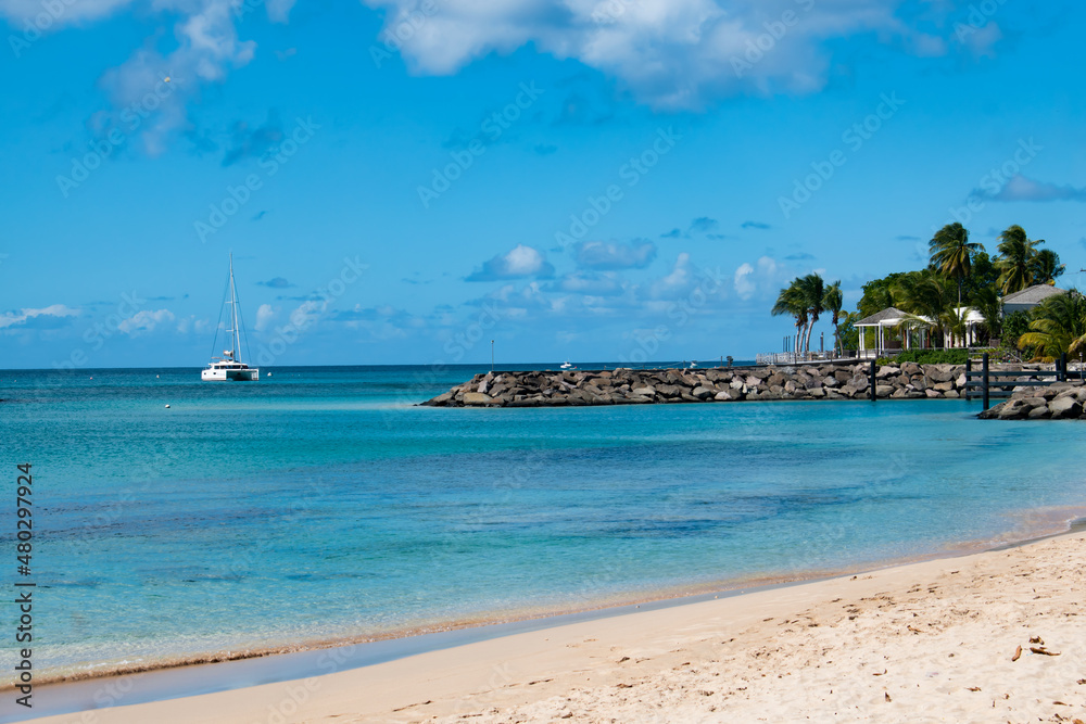 A beautiful view from a white sand beach on the island of Barbados with blue waters, a boat and palm trees.  Great for postcards.