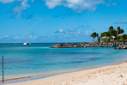 A beautiful view from a white sand beach on the island of Barbados with blue waters, a boat and palm trees. Great for postcards.